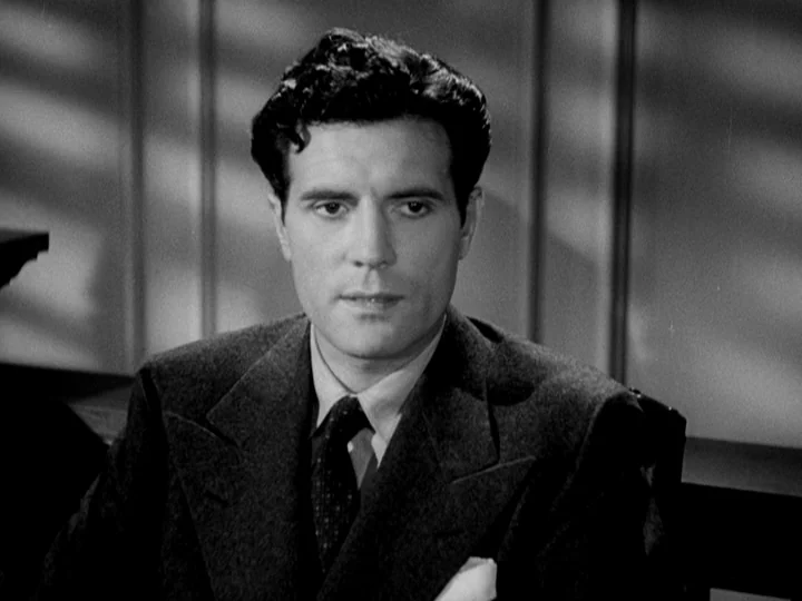 Stranger on the Third Floor (1940) movie still: medium — A man sits in an office with paneled walls marked by blind-filtered window light. He wears…