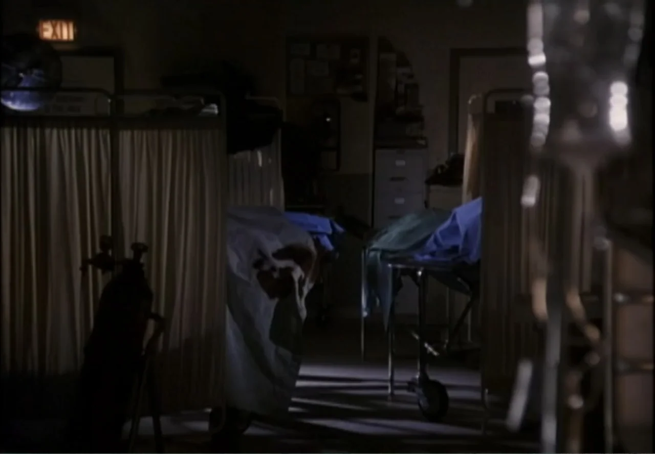 White Mile (1994) movie still: wide — A dimly lit hospital room features multiple gurneys separated by hanging white fabric curtains. No people are…