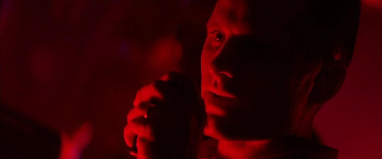 Crimson Tide (1995) movie still: closeup — A dimly lit room is illuminated entirely by intense red monochromatic lighting. A man stands holding a…