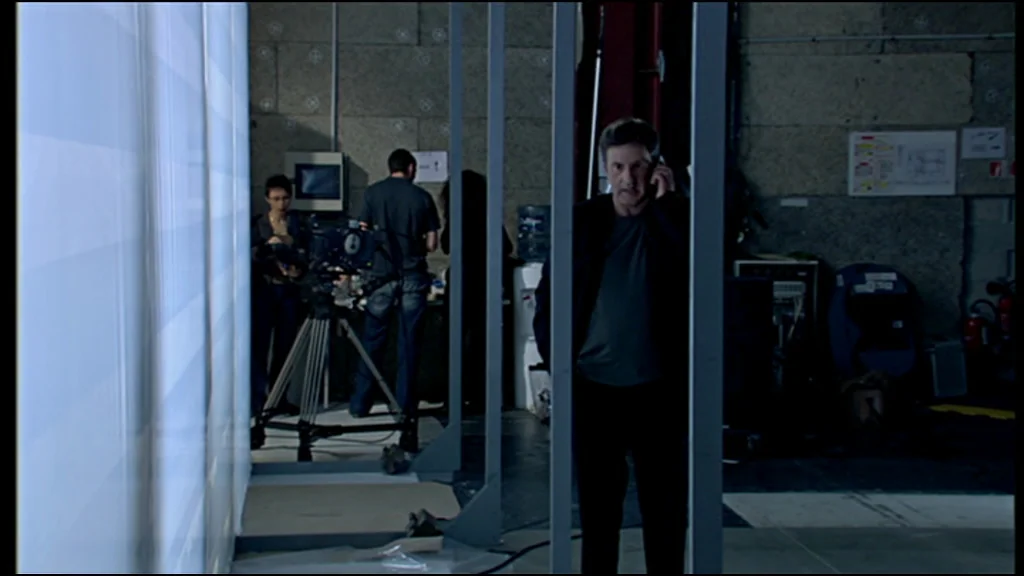 Caché (Hidden) (2005) movie still: medium — A utilitarian industrial space filled with production equipment and exposed concrete walls. A man in a…