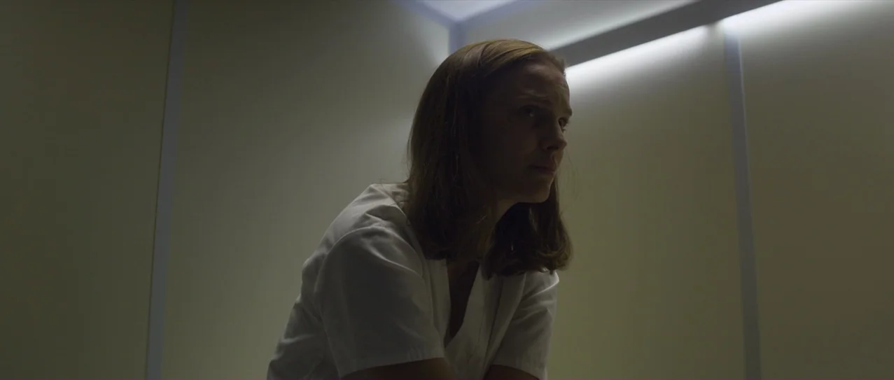 Annihilation (2018) movie still: medium — A spare medical room features blank off-white walls illuminated by concealed linear light fixtures. A…
