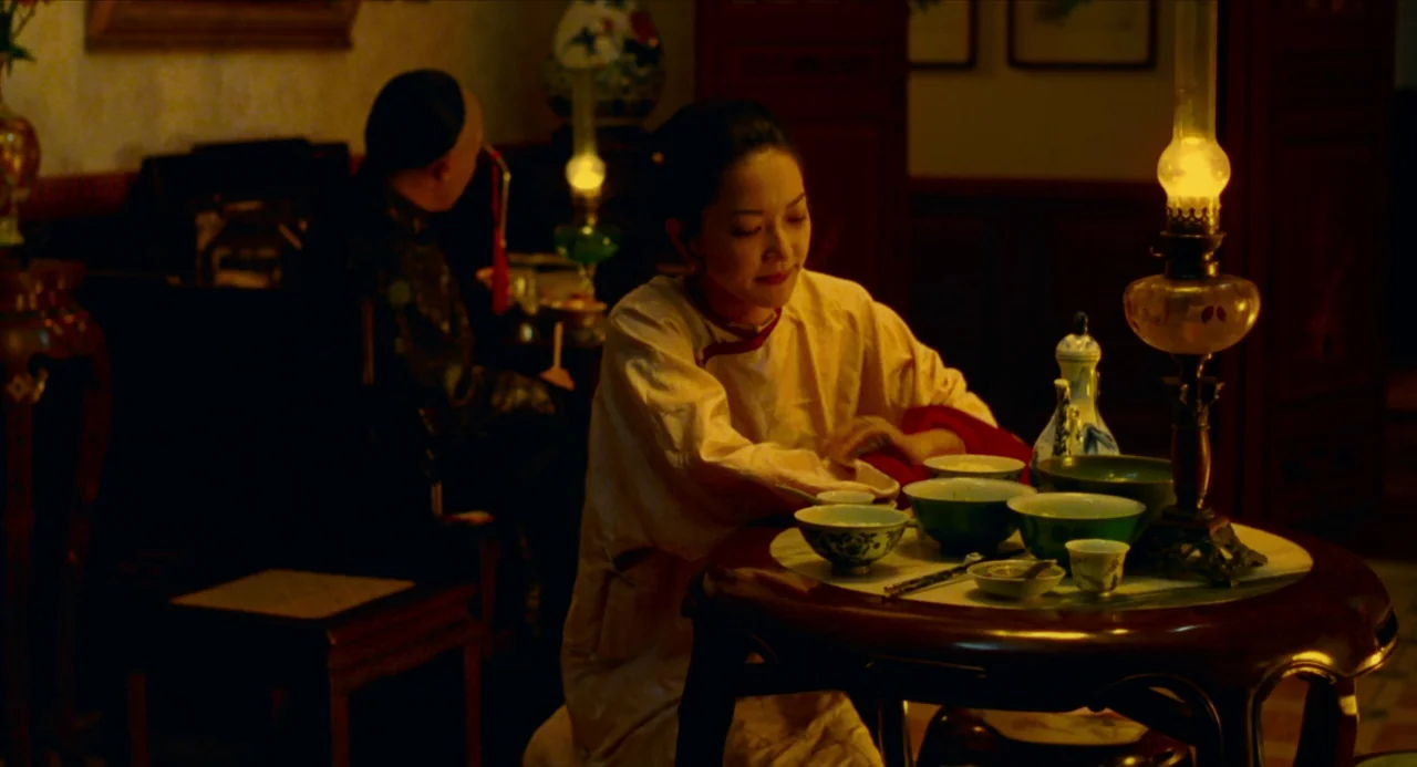 Flowers of Shanghai (1998) movie still: medium — An interior dining area dimly lit by antique oil lamps on wooden furniture. A woman in traditional…