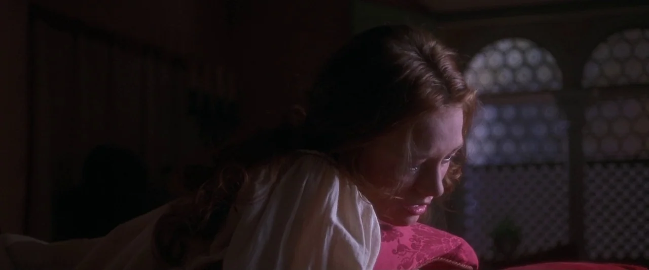 Dangerous Beauty (1998) movie still: closeup — A dim room features a window with a patterned, latticed light design. A woman with long auburn hair…