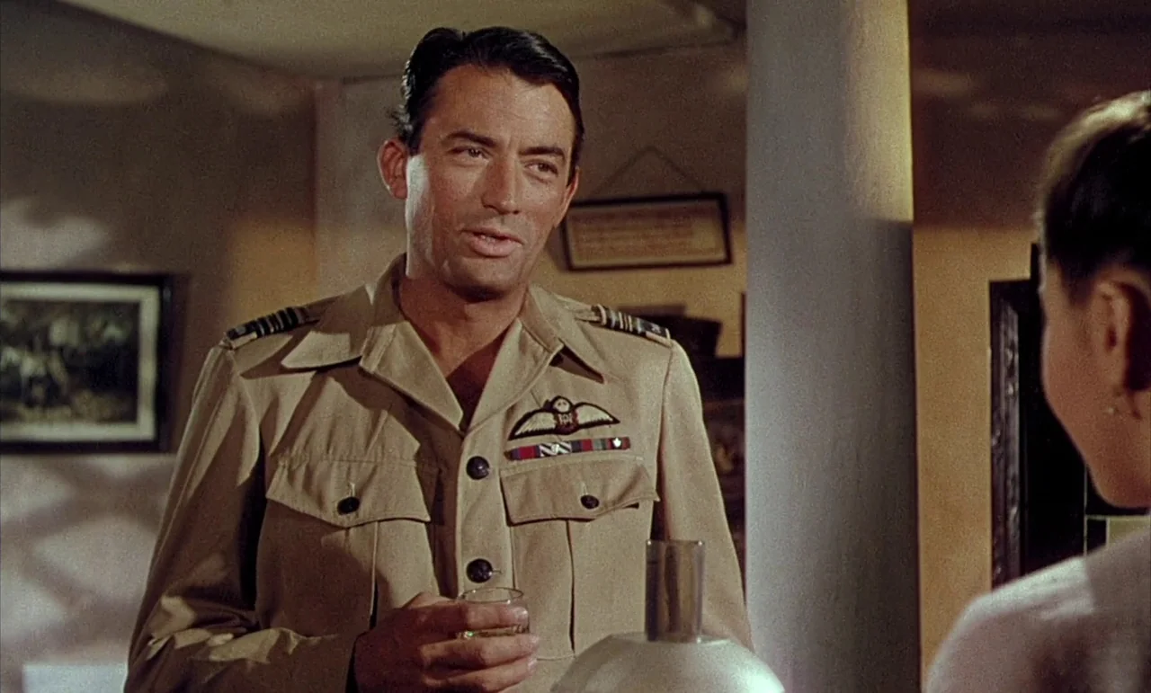 The Purple Plain (1954) movie still: medium — A domestic indoor space with a central column and framed artwork on the walls. A man in military…