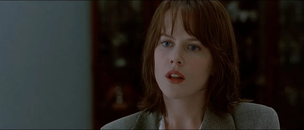 The Peacemaker (1997) movie still: closeup — A woman stands in a bright indoor workspace with blurred objects in the background. She faces slightly…