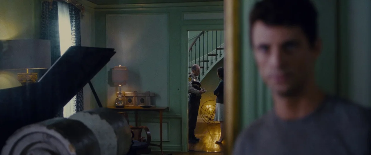 Stoker (2013) movie still: medium — A mint green room with crown molding features a piano and a view into a hallway. A police officer stands in the…