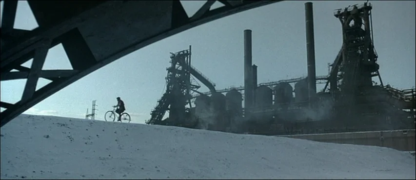 Road To Perdition (2002) movie still: wide — A desolate industrial site features large blast furnaces and a sandy, barren foreground. A lone…