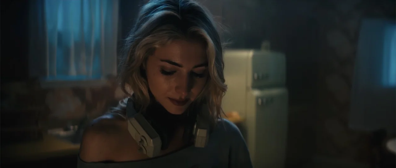 Night of the Missing (2023) movie still: closeup — A dimly lit room contains a retro refrigerator in the blurred background. A young woman with…