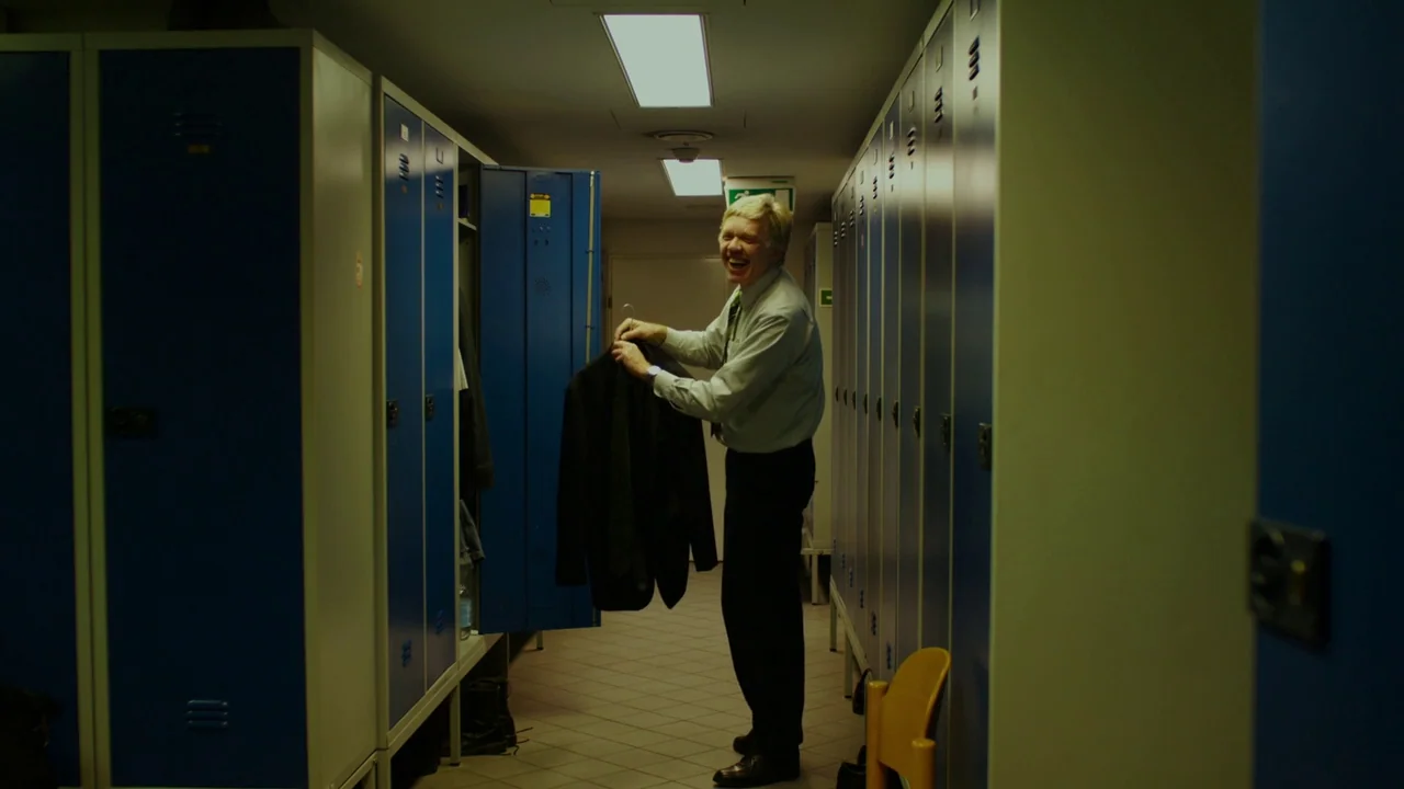 Museum Hours (2012) movie still: fullbody — A narrow corridor lined on both sides with tall blue metal storage lockers. A middle-aged man stands…