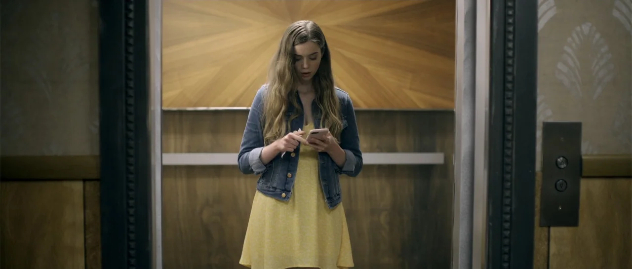 Elevator Game (2023) movie still: medium — An elevator interior features wood-paneled walls with a geometric star pattern inlay. A young woman…