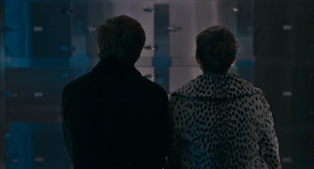 Restless (2011) movie still: medium — A sterile room featuring a wall of stainless steel doors for body storage. Two people stand with their backs…