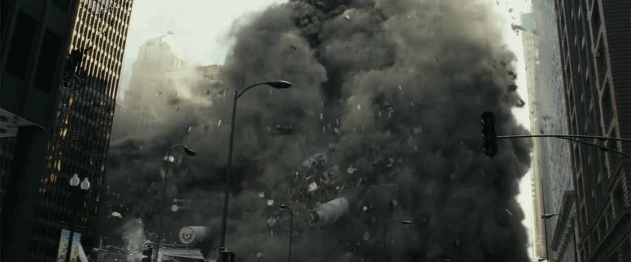 Rampage (2018) movie still: establishing — A dense cloud of dark smoke and rubble crashes through a busy downtown city street. Debris and pulverized…