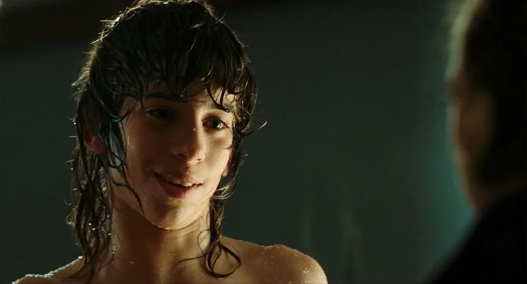 This Night (2008) movie still: closeup — A dimly lit indoor space with dark walls and wet surfaces. A young person with wet, messy hair looks toward…