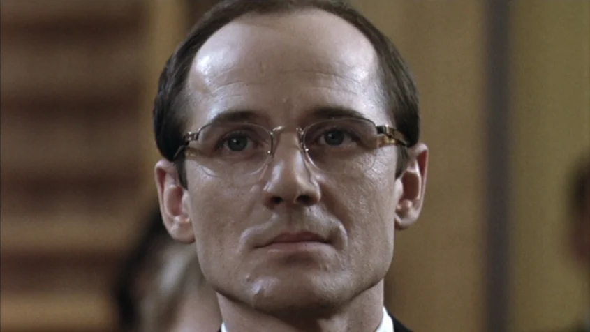 Benny’s Video (1992) movie still: closeup — A man stands in a courtroom with wood paneling in the background. The man looks directly into the camera…