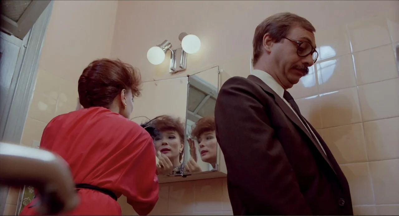 Waiting for the Hearse (1985) movie still: medium — A tiled interior wall features a medicine cabinet with mirrors and light fixtures. A woman…