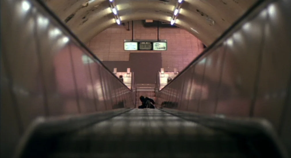An American Werewolf in London (1981) movie still: wide — An underground transit tunnel features a long metal escalator leading down toward a…