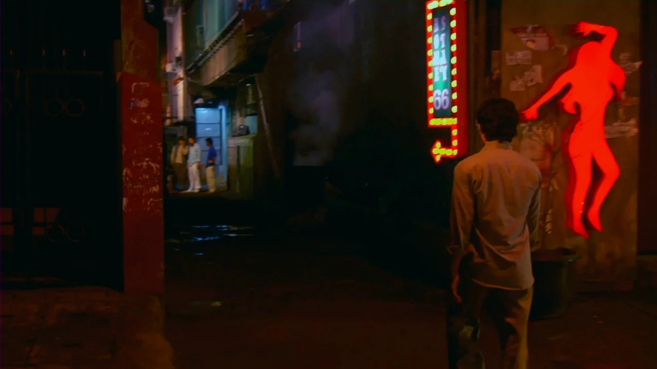 Merantau (2009) movie still: medium — A dimly lit narrow urban passageway features a glowing red neon silhouette on brick. A lone man in a light…