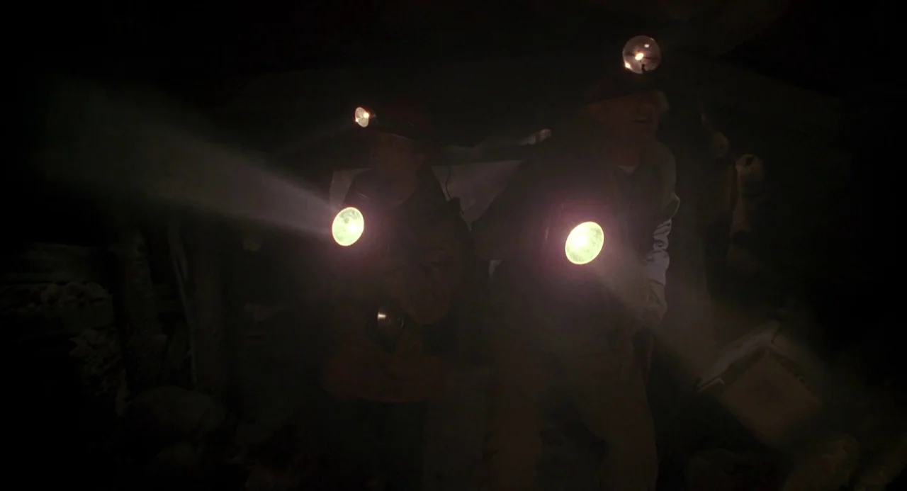 Back To The Future Part III (1990) movie still: medium — Two individuals navigate a dark, narrow underground passage with limited artificial light.…