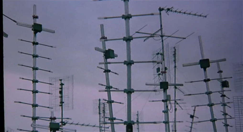 Intervista (1987) movie still: establishing — A rooftop crowded with multiple metal television antennas against a pale, overcast sky. The structures…
