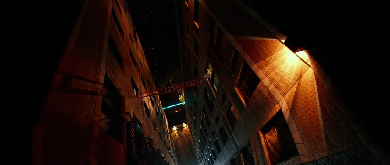 Nerve (2016) movie still: wide — Two towering brick buildings rise vertically, flanking a narrow night-time urban passage. A bright red ladder…