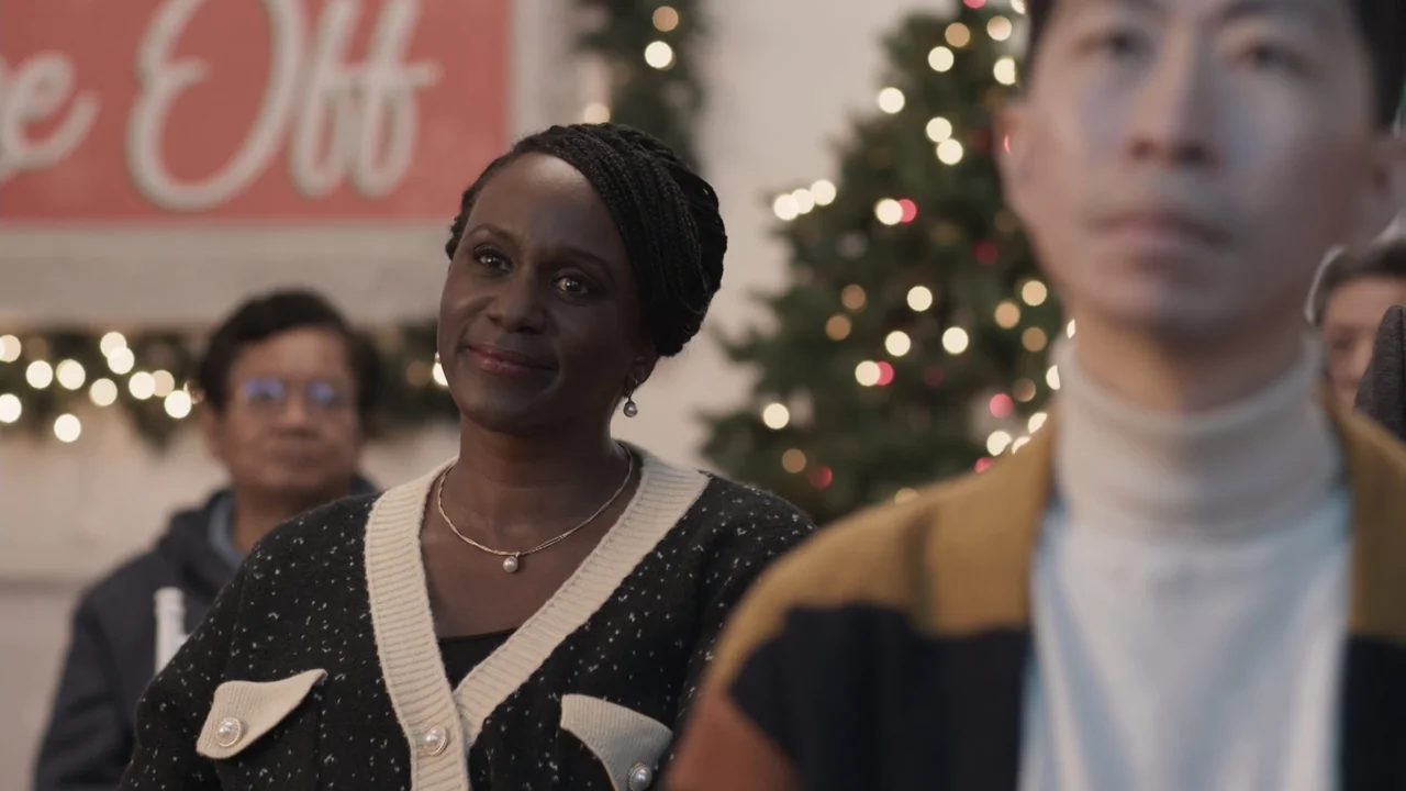 A Gingerbread Christmas (2022) movie still: medium — A festive indoor space is decorated for the holidays with soft focus greenery visible. A woman…