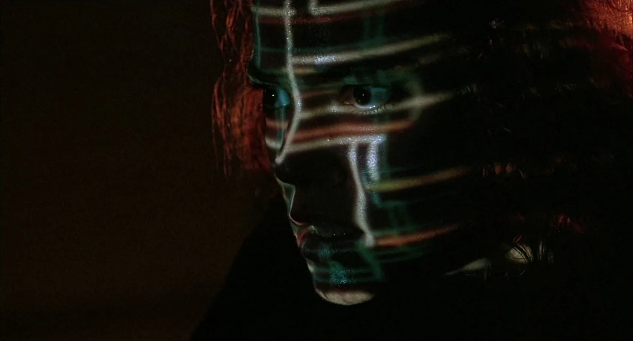 Hardware (1990) movie still: closeup — A dark environment surrounds a person in a dimly lit, undefined space. Complex geometric light lines are…