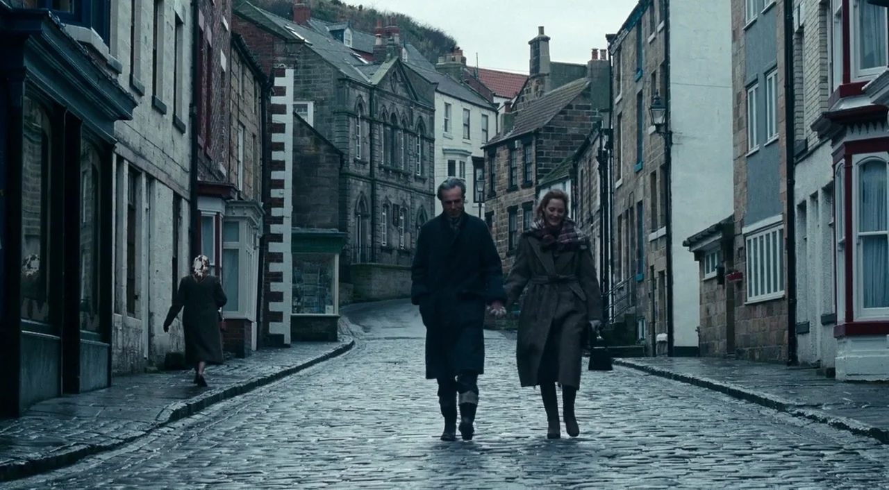 Phantom Thread (2017) movie still: fullbody — A historic, narrow European village street is paved with uneven wet cobblestones. A man and woman walk…
