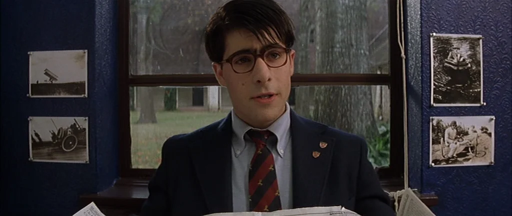 Rushmore (1998) movie still: medium — A study with deep blue walls featuring four black-and-white framed photographs. A young man wearing a blazer…