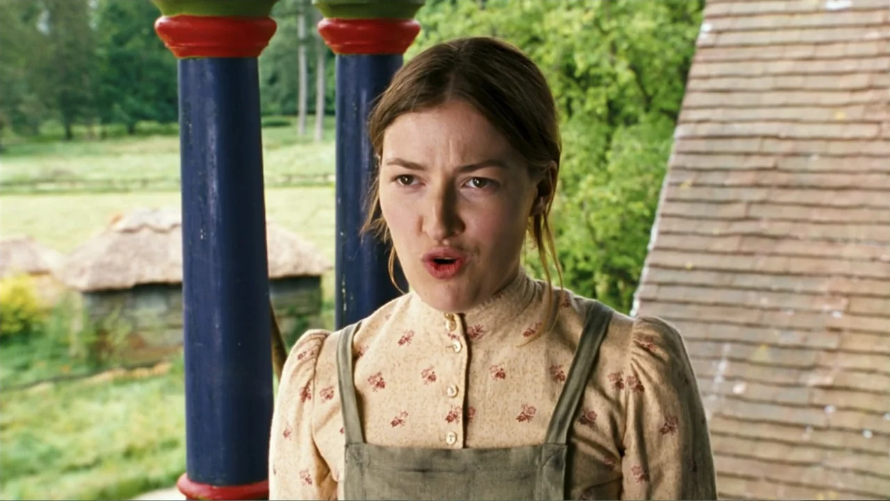 Nanny McPhee and the Big Bang (2010) movie still: medium — A woman stands on a porch with blue and red pillars in the countryside. She wears a…
