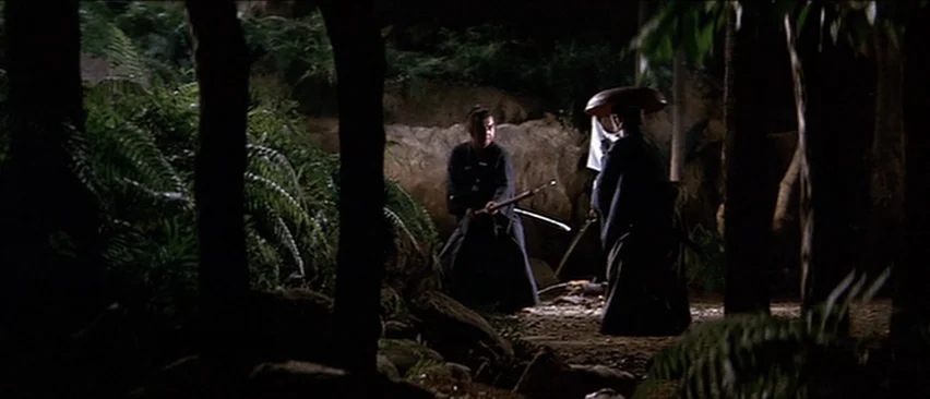 Lone Wolf and Cub: Baby Cart in the Land of Demons (1973) movie still: wide — A dark clearing in a dense forest surrounded by large trees and ferns.…