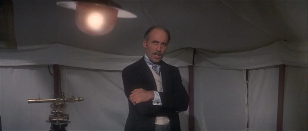 The Private Life of Sherlock Holmes movie still: medium — A beige canvas tent interior lit by a low-hanging warm lantern. A man stands in front of…