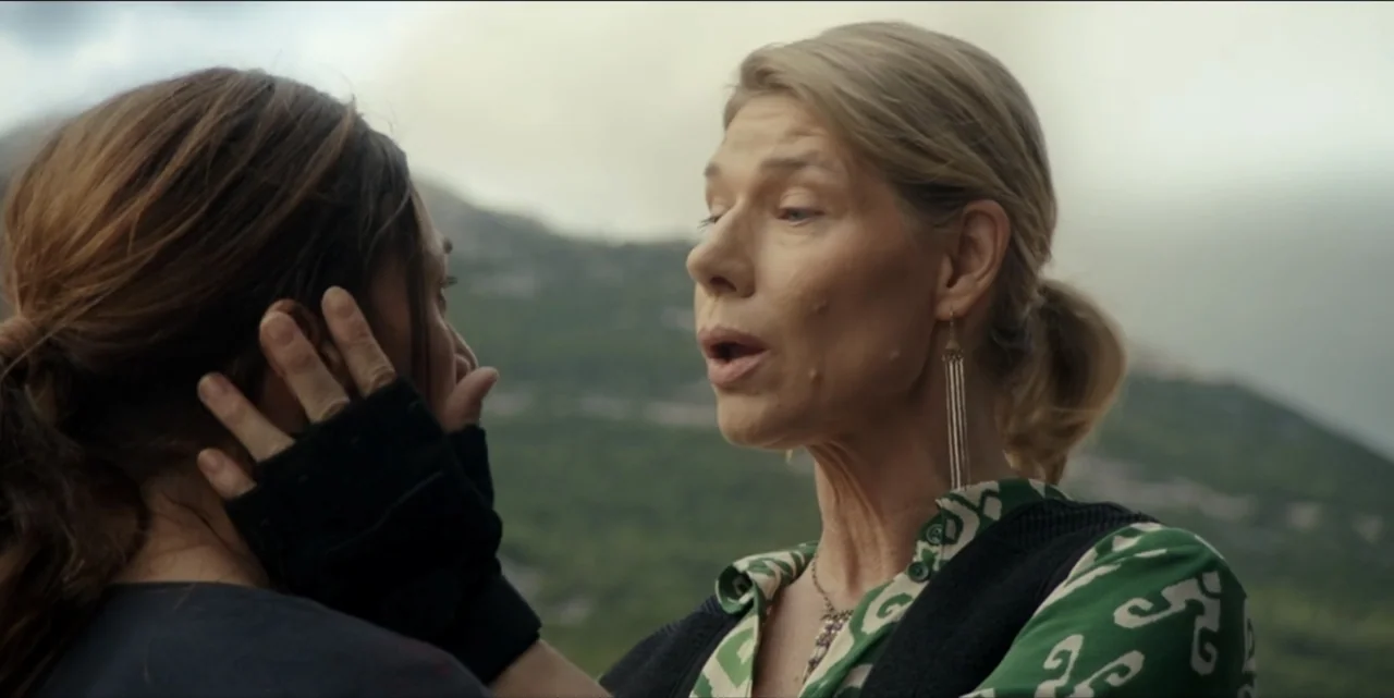 The Hunted (2024) movie still: medium — An outdoor mountainous landscape with rocky slopes provides the setting for the interaction. A woman in a…