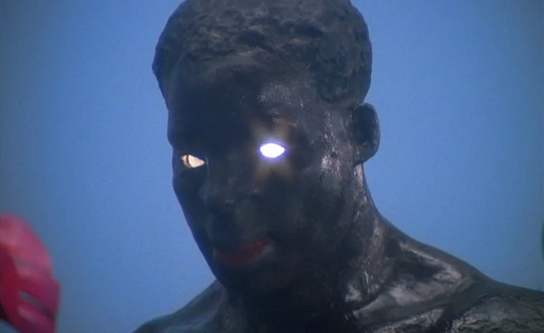 Sweet Movie (1974) movie still: closeup — A dark, blue-toned jungle night environment provides the backdrop for the glowing subject. A dark-skinned…