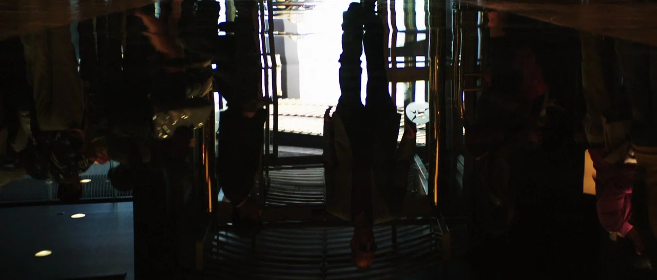 Rampart (2011) movie still: fullbody — A dark, highly polished floor reflects the silhouette of a man walking forward. The bright opening of an…