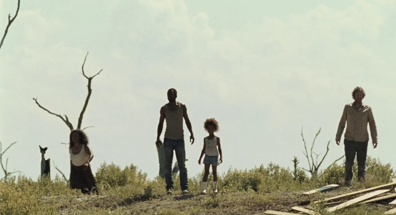 Beasts Of The Southern Wild (2012) movie still: wide — An open field under a bright, overcast sky features sparse, leafless dead trees. Four people…