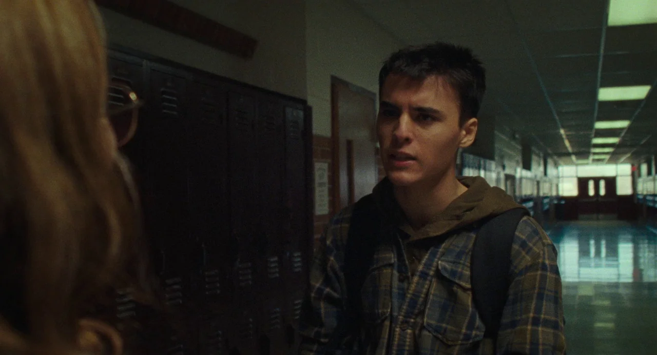 When You Finish Saving The World (2022) movie still: medium — A long school corridor lined with metal lockers stretches toward an exit door. A male…