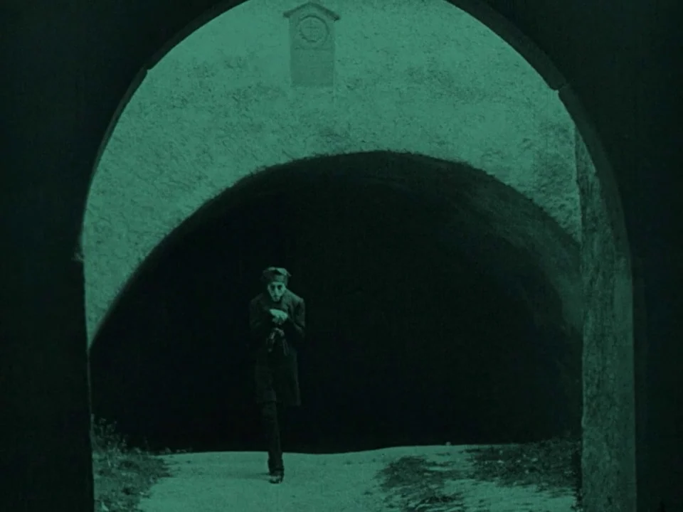 Nosferatu (1922) movie still: wide — A man walks towards the camera through the dark interior of a stone archway. An arched ceiling frames the…