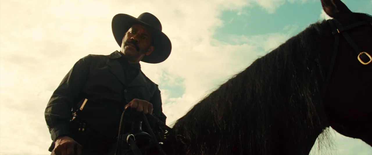 The Magnificent Seven (2016) (2016) movie still: medium — A man sits on a black horse against a bright, hazy sky. The scene shows the rider in a…