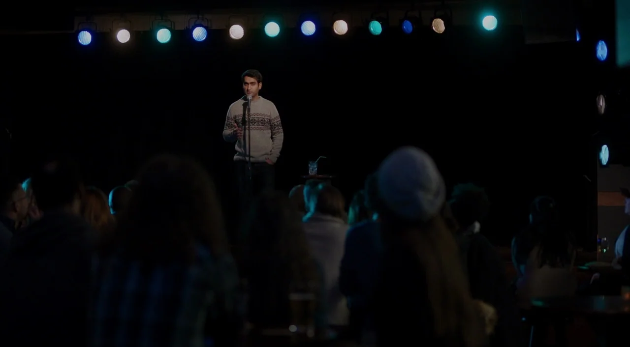 The Big Sick (2017) movie still: medium — A dark comedy club stage features a single performer against a black curtain. An audience sits in the…