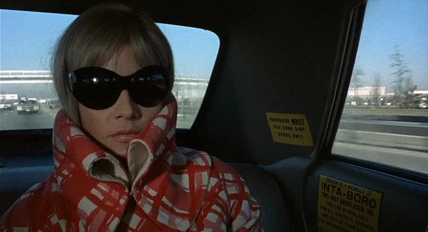 Perversion Story (1969) movie still: closeup — A woman sits in the back of a taxi travelling along a highway. The interior window displays yellow…
