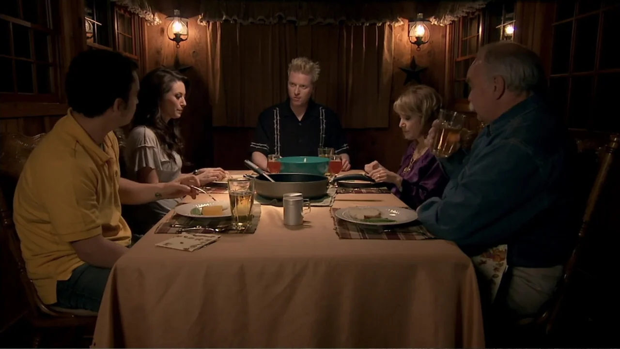 Hot Gimmick: Girl Meets Boy (2019) movie still: medium — A wood-paneled dining room contains a table set with multiple plates and glassware. Five…