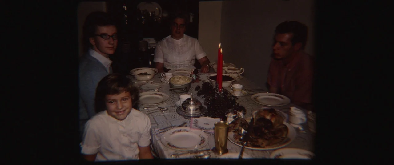 Nomadland (2020) movie still: medium — A family sits around a dining table set with white patterned plates and dishes. A roast chicken centerpiece…