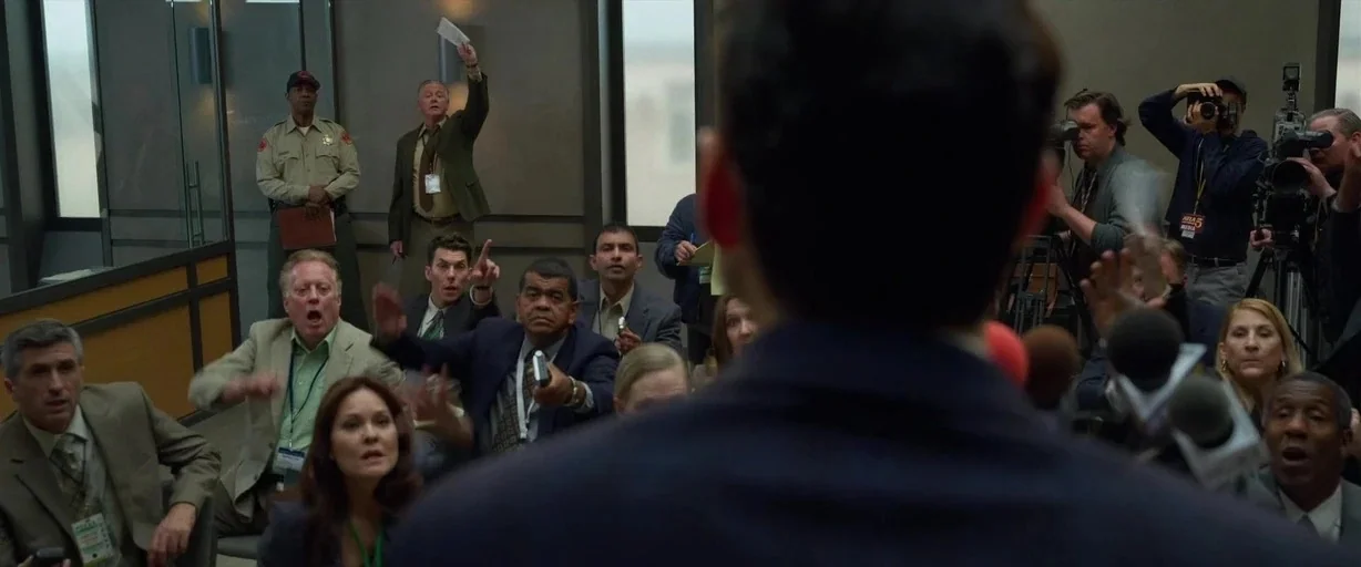 The Little Things (2021) movie still: medium — A modern, sterile conference room filled with various journalists and a uniformed officer.
