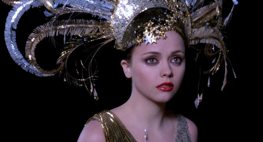 The Man Who Cried (2000) movie still: closeup — A woman stands in front of a dark, non-descript background wearing an ornate headdress. She wears a…