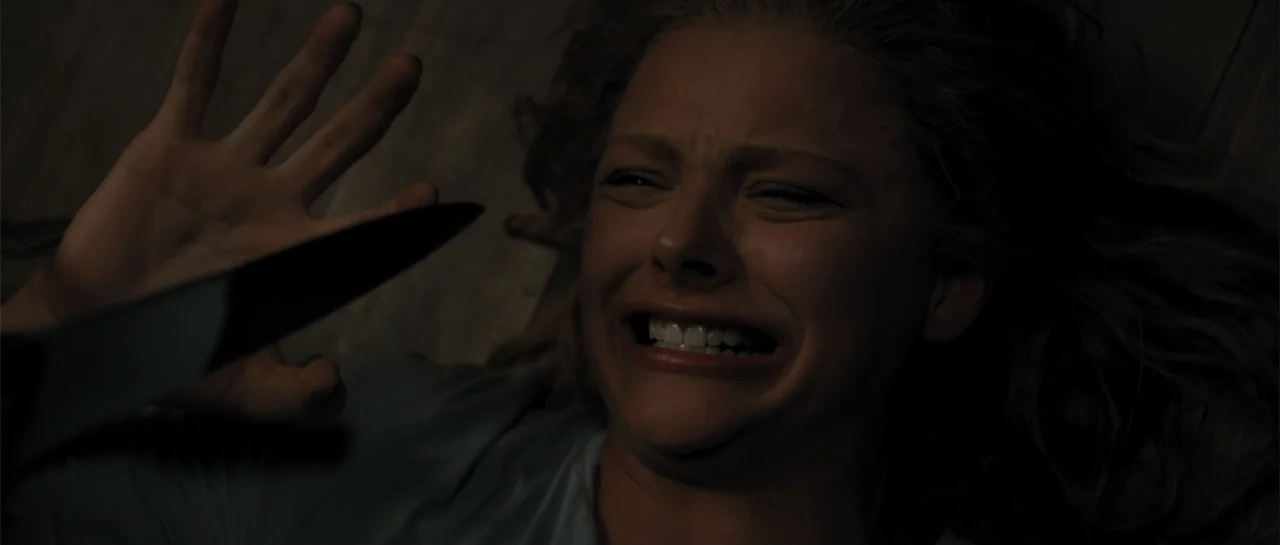 Carrie (2013) movie still: closeup — A dark bedroom interior features wooden floorboards seen from a high perspective. A young woman lies on her…