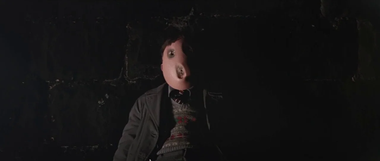 Pink Floyd The Wall (1982) movie still: medium — A dark space features a brick wall backdrop submerged in heavy shadow. A person wearing a smooth,…