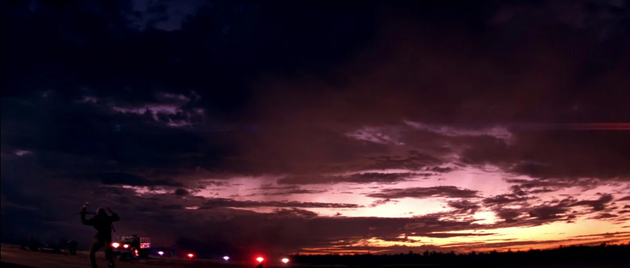 Born On The Fourth of July (1989) movie still: wide — A vast open airfield sits under a dramatic, dark purple and orange sunset sky. A solitary…