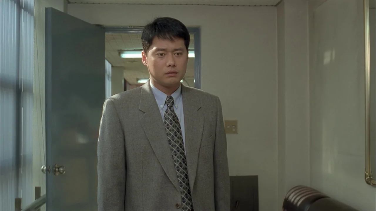 The Day a Pig Fell Into the Well (1996) movie still: medium — A plain interior hallway features off-white walls and an open grey metal doorway. A…