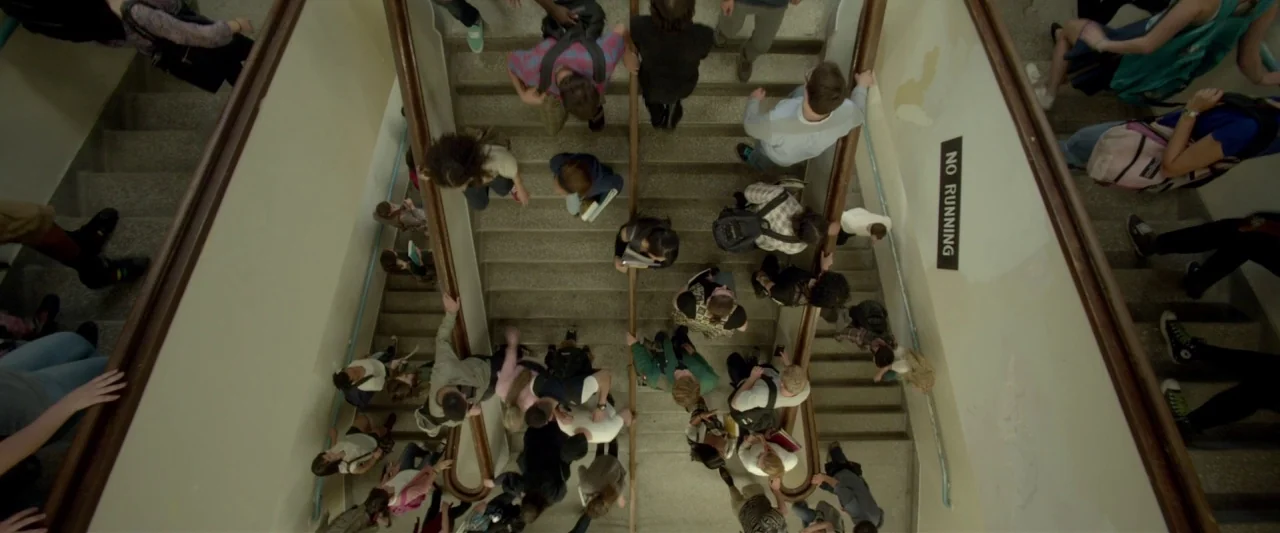 Me and Earl and the Dying Girl (2015) movie still: wide — A crowded school stairwell features two parallel concrete flights separated by a metal…