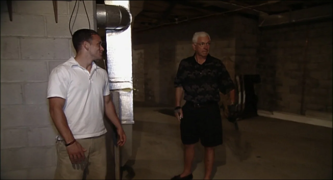 Hard as Nails (2001) movie still: fullbody — An unfinished concrete basement with exposed metal ductwork and cinder block walls. Two men stand in…